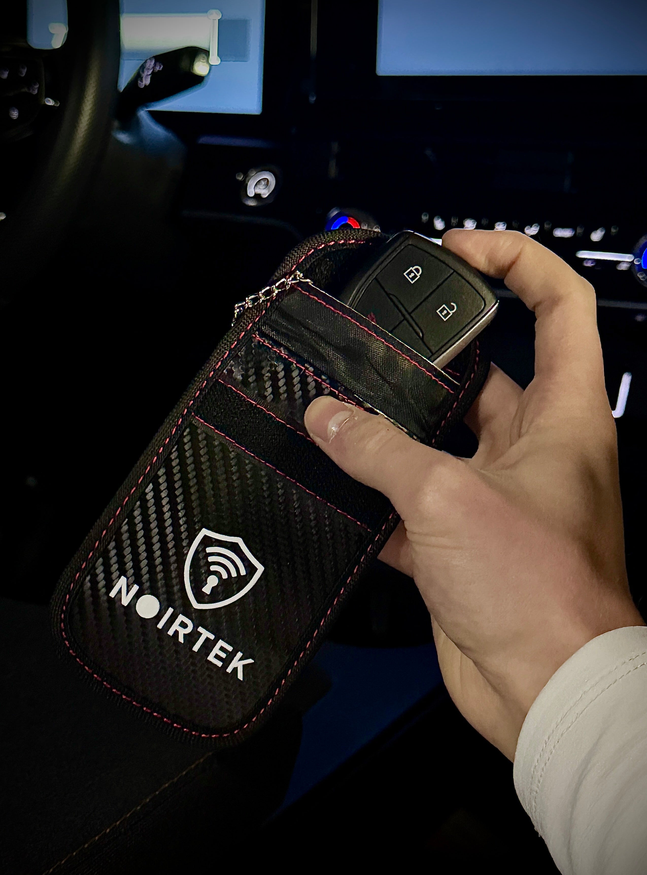 Hand holding a car key fob case with NOIRTEK branding inside a vehicle.